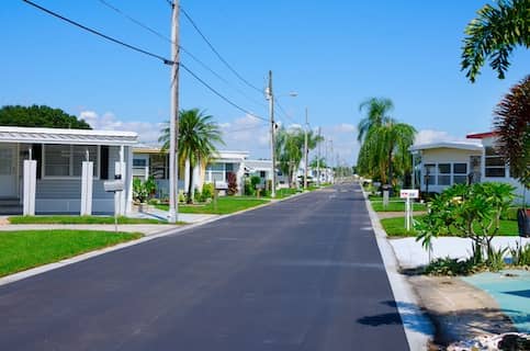 Neighborhood of colorful manufactured homes lining a palm tree-lined street.