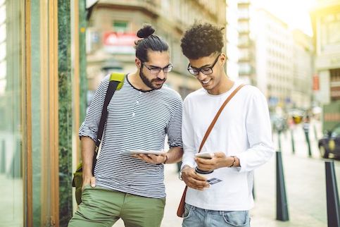 Two men walking on street looking at phone.