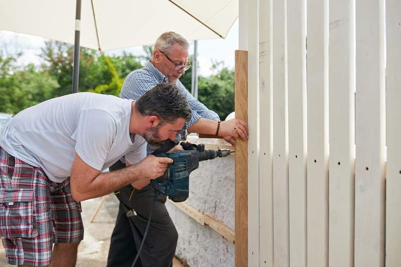 Two men work on a fence, one of the repairs that qualifies for an escrow holdback.