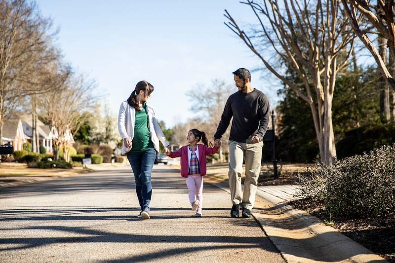 A woman and a man hold hands with their daughter as they walk down a safe neighborhood street.