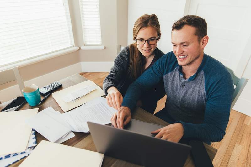 A young married couple works on a laptop, with mortgage documents spread out on the table.