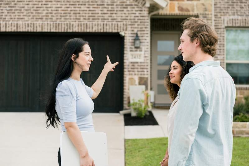 A real estate agent describes a home's exterior features to a young couple.