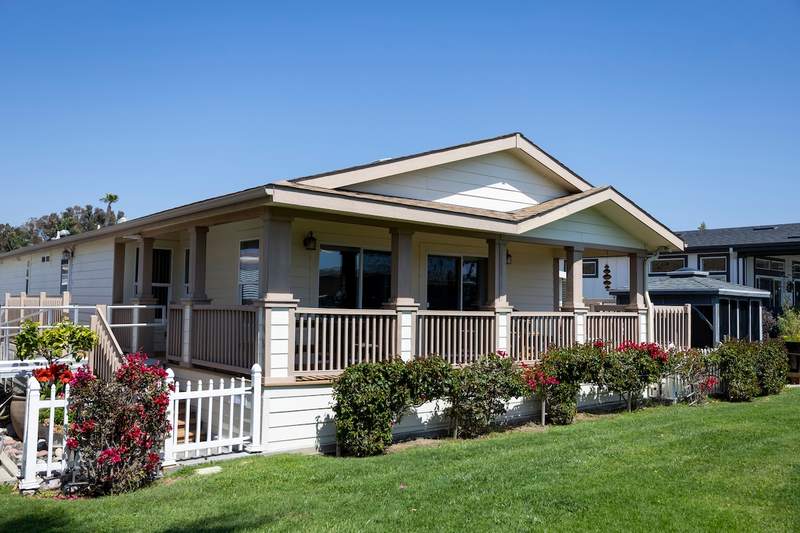 View of a manufactured home with a porch and garden on a sunny day.