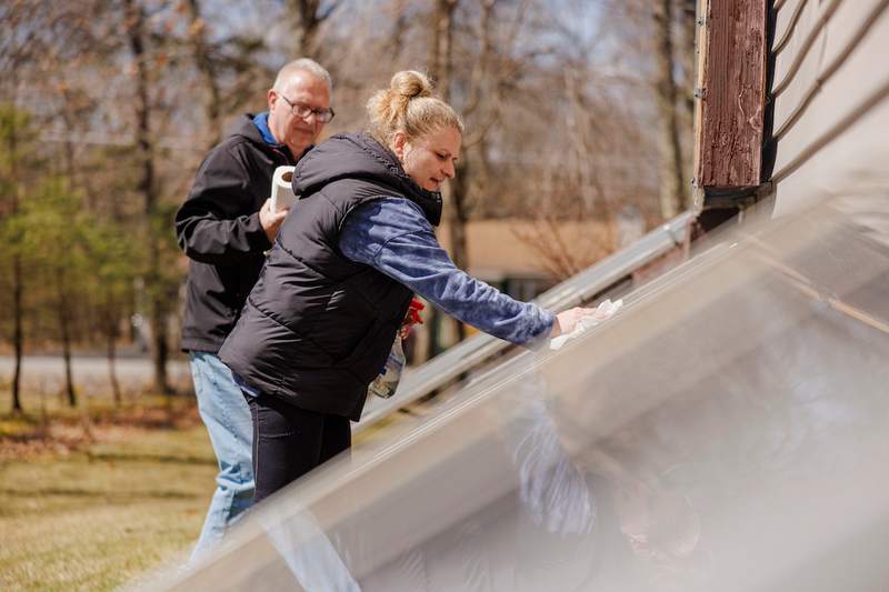 A man and woman clean the solar panels on their energy-efficient home.