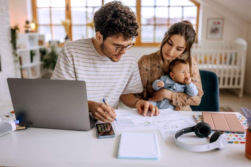 A couple with a baby sitting at a table in their apartment budgets for a new house.