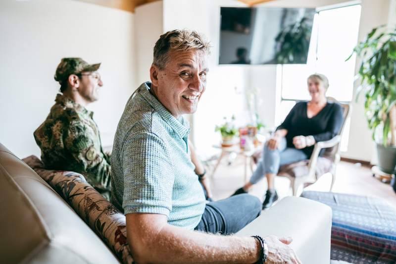 A veteran sits in the living room of a house with his mother and smiling father.