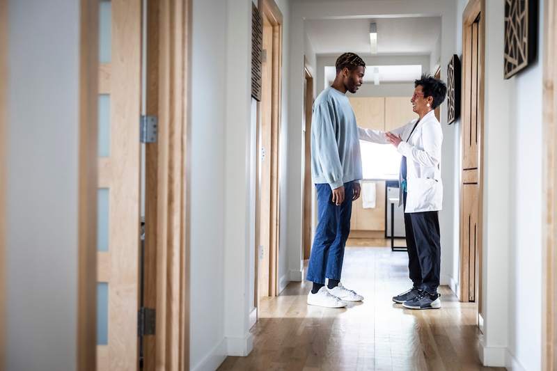 A female doctor talks to her son in the hallway of their home.