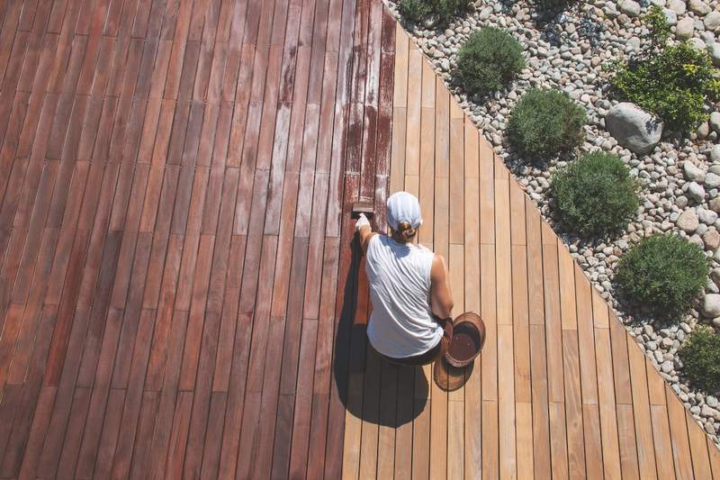 A homeowner applies stain to the wood of her house's deck.