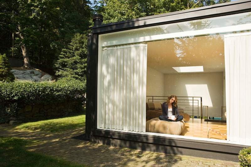 A woman sits in a modular home looking out a large window.